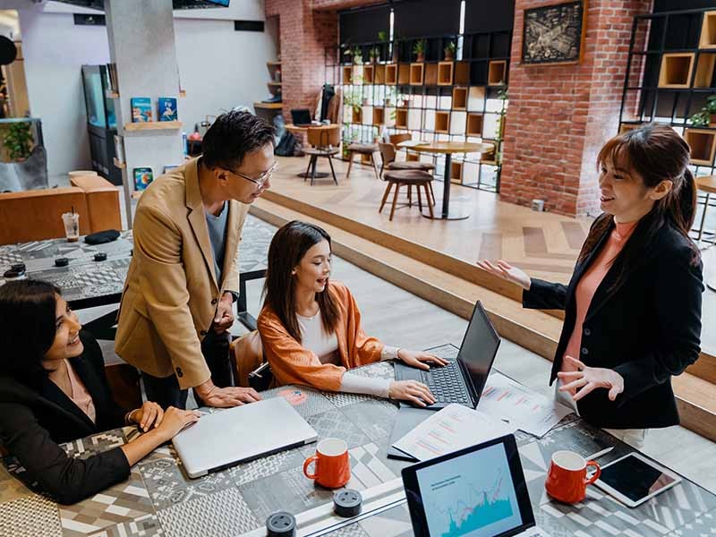 One man and three ladies in a collaborative office space, having a work group discussion 