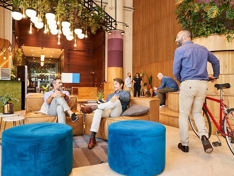 A group of people relaxes on couches in a lobby, with a bicycle parked nearby.