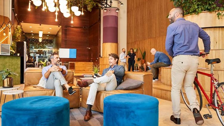 A group of people relaxes on couches in a lobby, with a bicycle parked nearby.